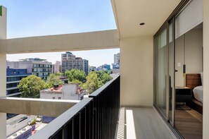 A balcony with a city view, a bed with a wooden headboard, and a nightstand with a lamp. - w Deluxe 2BR w Private Terrace in Hipodromo (Mexico City)