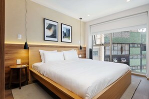 A modern hotel room with a large bed, two framed pictures on the wall, a small side table, and a large window with a view of buildings. - w Deluxe 2BR w Private Terrace in Hipodromo (Mexico City)