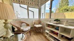 Un coin lecture confortable avec des fauteuils en osier, une table en verre et une bibliothèque remplie de livres.