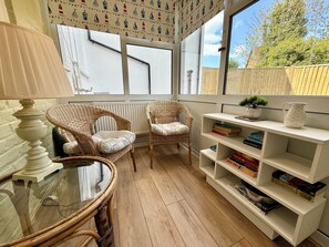 A cozy reading nook with wicker chairs, a glass table, and a bookshelf filled with books. - Downs Gate Cottage, Meads Village - Coast & South Downs On Your Doorstep (Eastbourne)