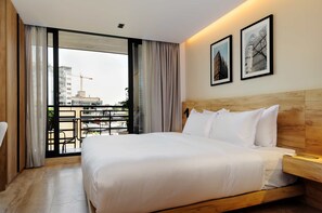 A hotel room with a large bed, a wooden headboard, a nightstand, and a view of a cityscape with buildings and a crane. - w Urban Loft W/balcony in Parque Mexico (Mexico City)