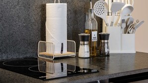 Eine Küchenarbeitsplatte mit Papierhandtuchhalter, einer Olivenölflasche, einer Gewürzglasmischung und einem Besteckbehälter.