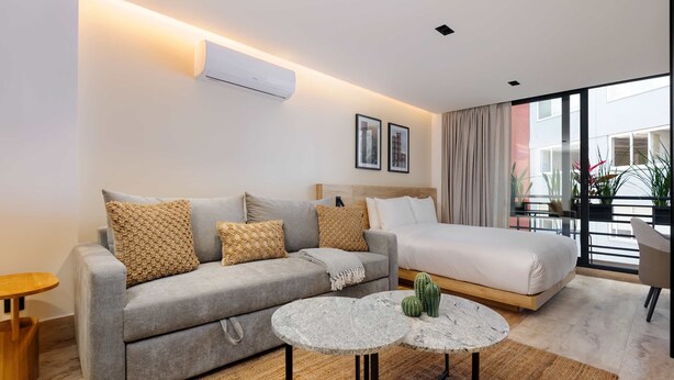 A modern hotel room with a grey sofa, a single bed, a small round table, and a large window with a view. - w Stylish Loft w/ Balcony in Parque Mexico (Mexico City)