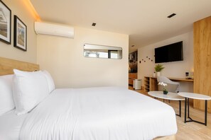 Moderni hotellihuone, jossa on suuri sänky, pieni pöytä, tuoli, televisio ja peili.