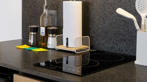 Una encimera de cocina con una placa de inducción negra, una botella de aceite de oliva, un dispensador de toallas de papel y utensilios de cocina.