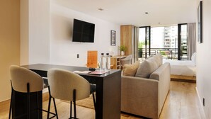 Una sala de estar moderna con un sofá, una mesa de comedor con sillas, un televisor de pantalla plana montado en la pared y un balcón con vistas a la ciudad.