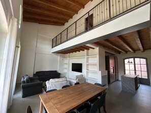 Ein geräumiger Wohnbereich mit Esstisch aus Holz, Sofas, einem Fernseher und einem Balkon mit Geländer.