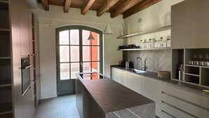 A modern kitchen with a marble island, wooden beams, and built-in appliances. - w Luxury 5BR Retreat Near Navigli (Milan)