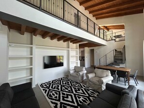 A spacious living area with a high ceiling, built-in shelves, a flat-screen TV, a patterned rug, and a dining area with a table and chairs. - w Luxury 5BR Retreat Near Navigli (Milan)