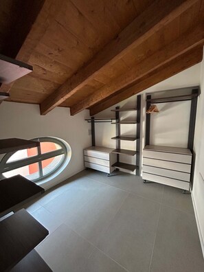 Ein Zimmer mit schrägem Dach, einem Fenster und integrierten Regaleinbauten.
