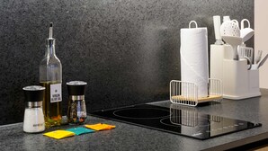 En köksbänk med en svart induktionshäll, en flaska olivolja, en behållare med salt, en pepparkvarn och en hållare för hushållspapper med diverse köksredskap.