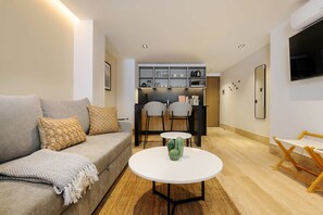 Ein modernes Wohnzimmer mit einer Couch, einem Couchtisch und einem Essbereich mit Stühlen sowie einer Küche im Hintergrund.