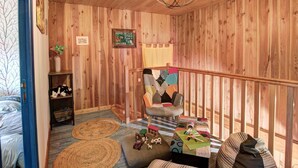 Un interno in legno con un letto, una poltrona, una sedia, una lampada a sospensione e una piccola mensola.