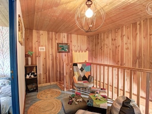 A wooden interior with a bed, a sofa, a chair, a hanging light fixture, and a small shelf. - Authentic cottage, pets welcome - 8 guests (Vêtre-sur-Anzon)