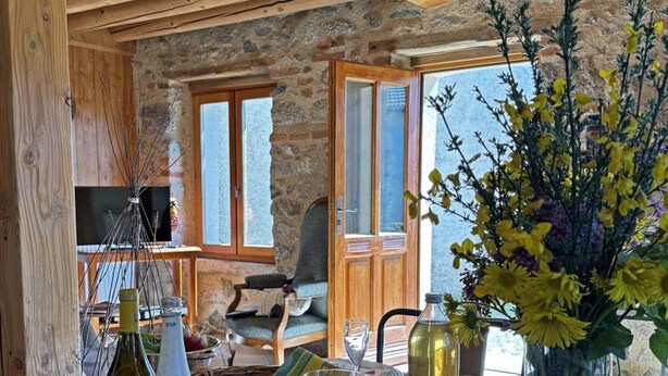 Un interno rustico con pareti in pietra, mobili in legno, un tavolo da pranzo con una candela e un vaso di fiori.
