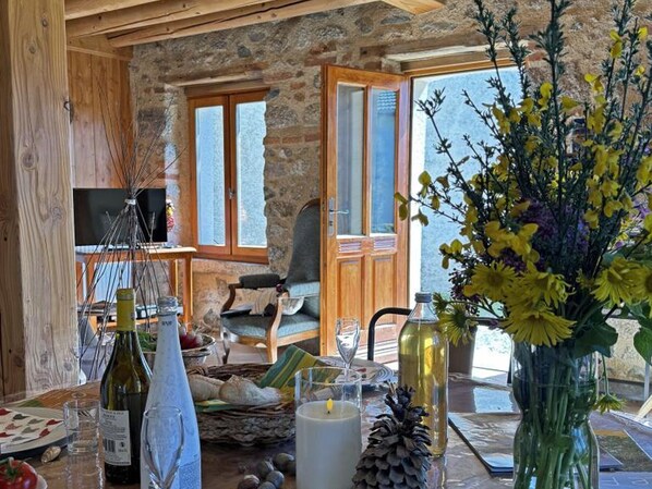 A rustic interior with stone walls, wooden furniture, a dining table with a candle, and a vase of flowers. - Authentic cottage, pets welcome - 8 guests (Vêtre-sur-Anzon)