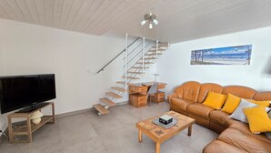 Una sala de estar moderna con un televisor de pantalla plana, una mesa de centro de madera, un sofá de cuero marrón, un escritorio con una silla y una escalera.