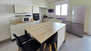 Una cocina moderna con armarios blancos, una mesa de madera, sillas negras, un microondas, un horno, un fregadero y un refrigerador.