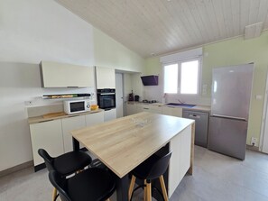 Eine moderne Küche mit weißen Schränken, einem Holztisch, schwarzen Stühlen, einer Mikrowelle, einem Backofen, einer Spüle und einem Kühlschrank.