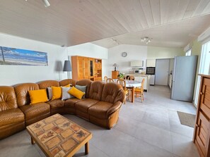 Ein Wohnzimmer mit braunem Ledersofa, einem Holztisch und einem Essbereich mit weißem Tisch und Stühlen.