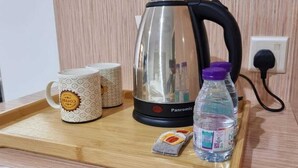 A wooden tray with a kettle, two patterned mugs, a water bottle, and a tea packet. - Delta Park Serviced Apartments (Riyadh)