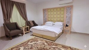 A bedroom with a bed, a chair, a small table, and a decorative wall panel. - Delta Park Serviced Apartments (Riyadh)