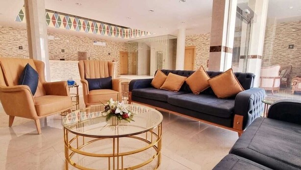 A modern hotel lobby with a sofa, armchairs, a glass coffee table, and a decorative flower arrangement. - Delta Park Serviced Apartments (Riyadh)