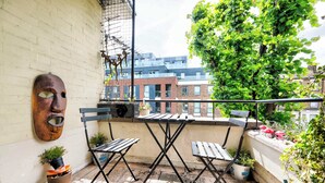 A balcony with a table and chairs, potted plants, a metal sculpture, and a view of buildings. - The Explorer's Home (Greater London)
