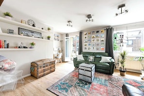 Ein Wohnzimmer mit einem grünen Sofa, einem alten Koffer und einem gemusterten Teppich.