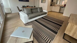 En moderne stue med en grå sofa, et spisebord og en bærbar computer på et mønstret gulvtæppe.