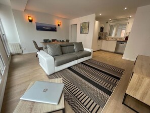 Ein modernes Wohnzimmer mit grauem Sofa, einem Esstisch und einem Laptop auf einem gemusterten Teppich.