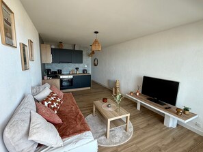 A modern living room with a sofa, a coffee table, a TV, and a kitchen in the background. - Studio sea view, pets allowed (Saint-Jean-de-Monts)