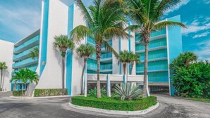 Ein modernes Hotel mit blauer und weißer Fassade, mehreren Etagen und Palmen im Vordergrund.