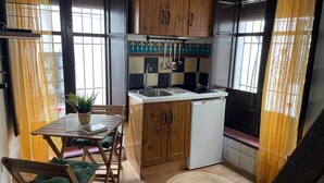 A compact kitchen with wooden cabinets, a white refrigerator, a sink, and a dining table with chairs. - Bright studio in Albaicín - 2 guests (Granada)