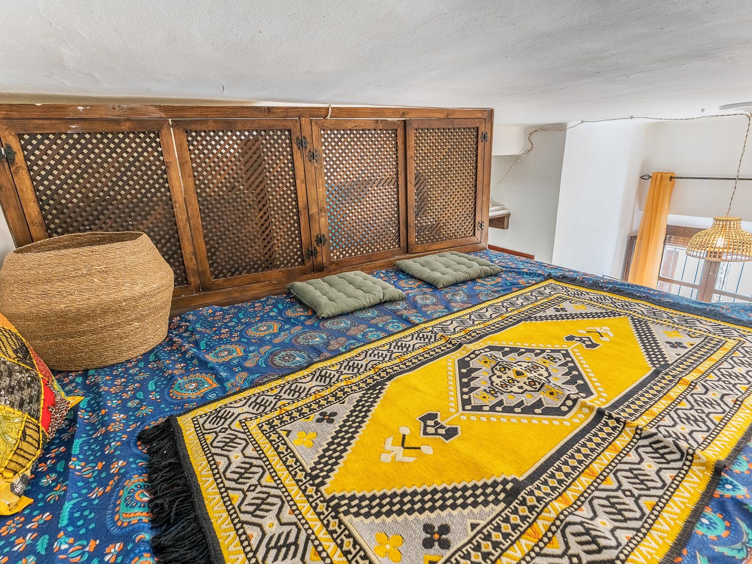 Une pièce dotée d’un tapis à motifs, d’un pouf en fibres tressées et d’une cloison en bois ornée d’un motif en treillis.