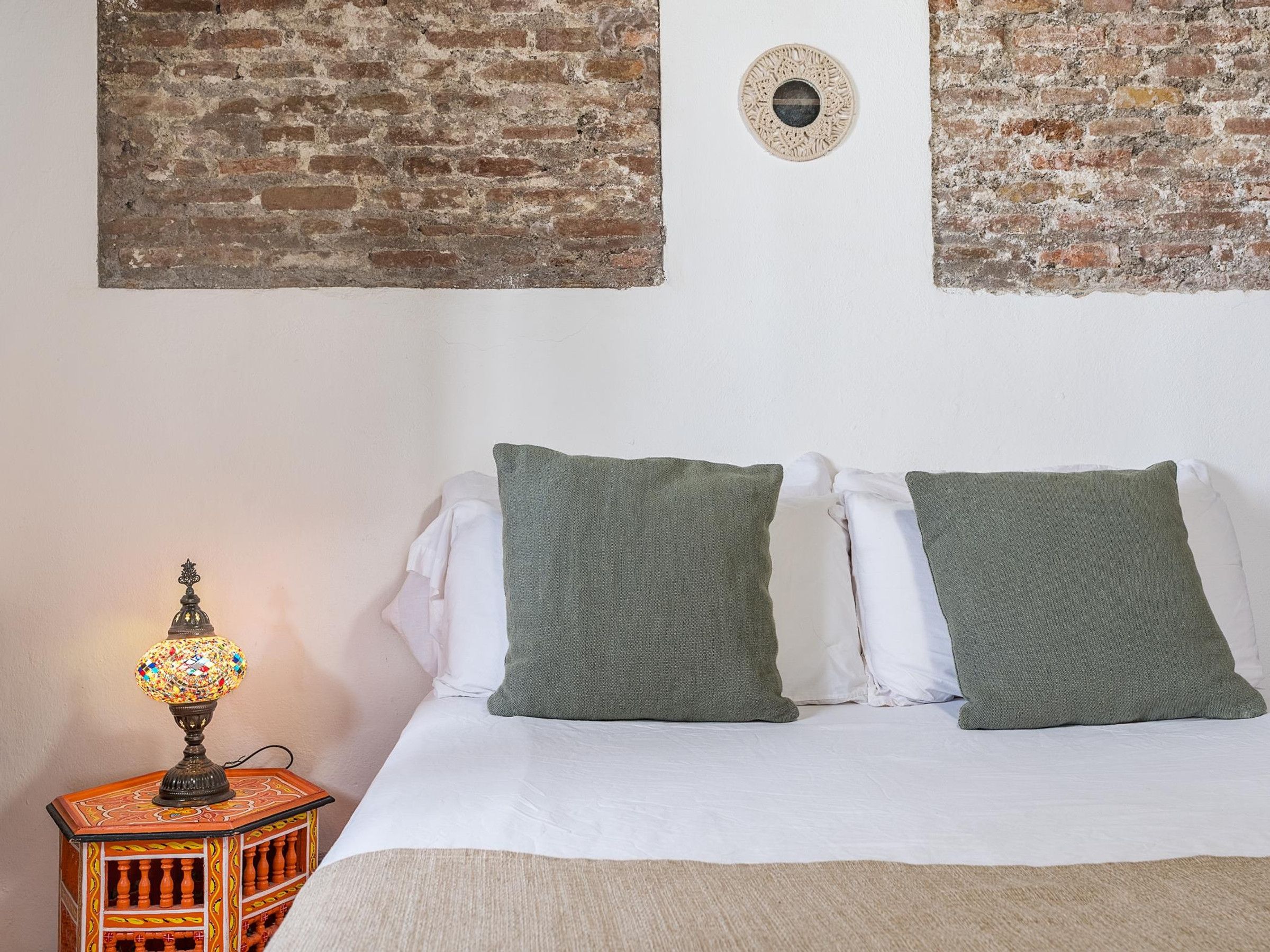 A bed with two pillows, a lamp, and a wall with a brick pattern and a circular decoration.