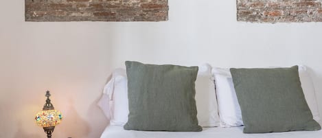 A bed with two pillows, a lamp, and a wall with a brick pattern and a circular decoration.