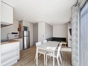 A compact kitchen with a refrigerator, microwave, and a dining area with a table and chairs. - Mobile home with parking, pets welcome - 4 guests near beach (Jullouville)