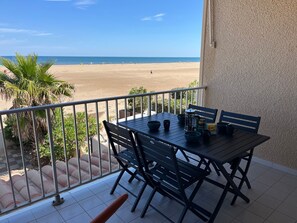 A balcony with a table and chairs overlooking a beach. - Apartment with sea view, pool, parking - 6 guests (Gruissan)