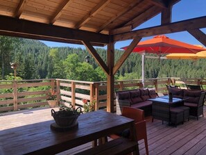 Une terrasse en bois avec des sièges d’extérieur, une table et une vue sur une zone boisée.