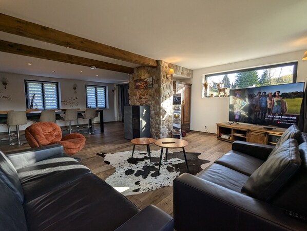 Ein modernes Wohnzimmer mit einer Steinsäule, Ledersofas, einem Fernseher und einem Essbereich mit Stühlen und einem Tisch.