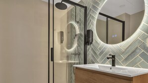 Un baño moderno con cabina de ducha de vidrio, tocador de madera y un salpicadero de azulejos con motivo de espiga.