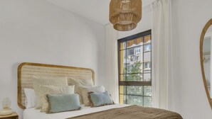 Un dormitorio con una cama grande, cabecera de mimbre, ventana con vistas y una lámpara colgante.