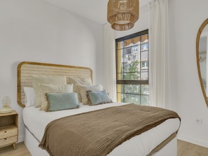 Ein Schlafzimmer mit einem großen Bett, einem Rattan-Kopfstück, einem Fenster mit Blick und einer Pendelleuchte.