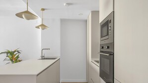 Una cocina estrecha con encimera blanca, electrodomésticos de acero inoxidable e iluminación colgante.