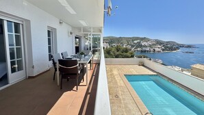 Un balcón con una mesa y sillas, una piscina y vistas al mar y las colinas.