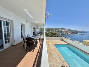 Ein Balkon mit Esstisch und Stühlen, ein Pool und Blick auf das Meer und die Hügel.