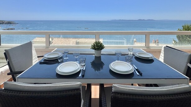 Una mesa para cuatro con vistas al mar, una planta en maceta y sillas de mimbre.