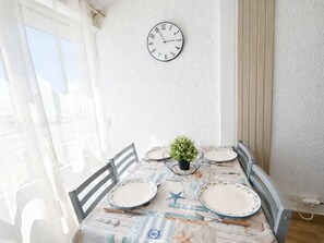 A dining area with a table set for four, a wall clock, and a window with curtains. - Peaceful studio near beach - 4 guests (Narbonne)