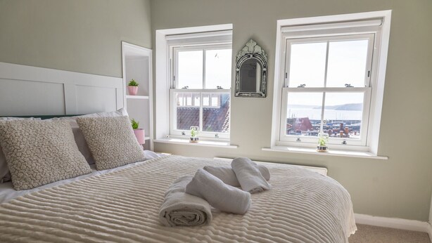 Een slaapkamer met een bed, twee ramen, een spiegel en uitzicht op een jachthaven.